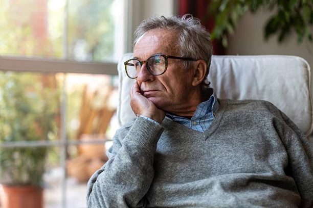 How to Manage Parkinson’s Nighttime Symptoms? The picture shows a senior with Parkinson's looking outside the window while sitting on his couch chair